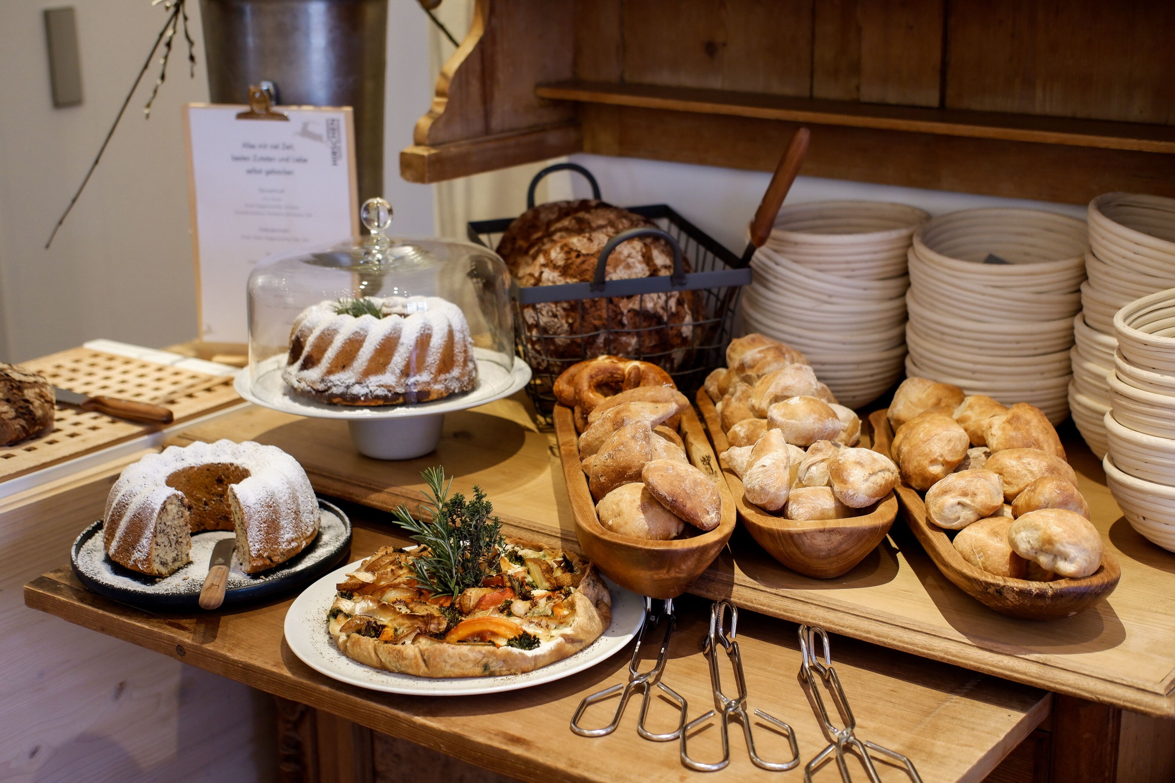 A buffet table with various baked goods, including a bundt cake, bread rolls, and a pizza.