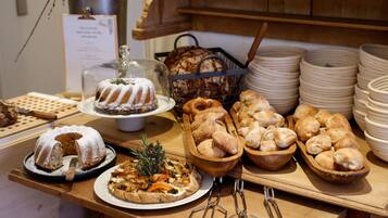 A buffet table with various baked goods, including a bundt cake, bread rolls, and a pizza.