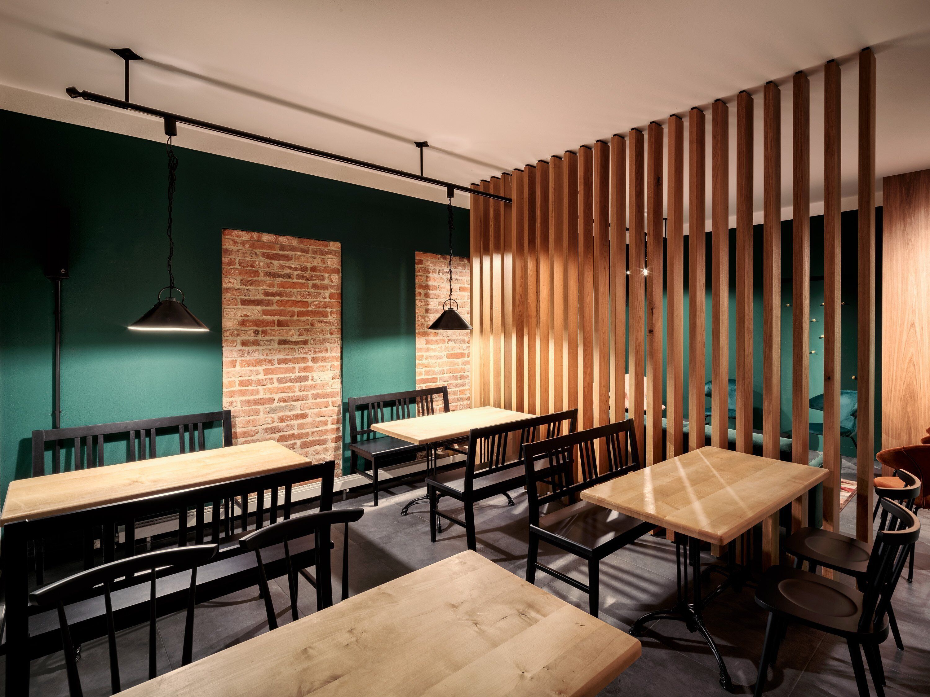 A modern dining area with wooden tables and benches, brick walls, and a green accent wall.