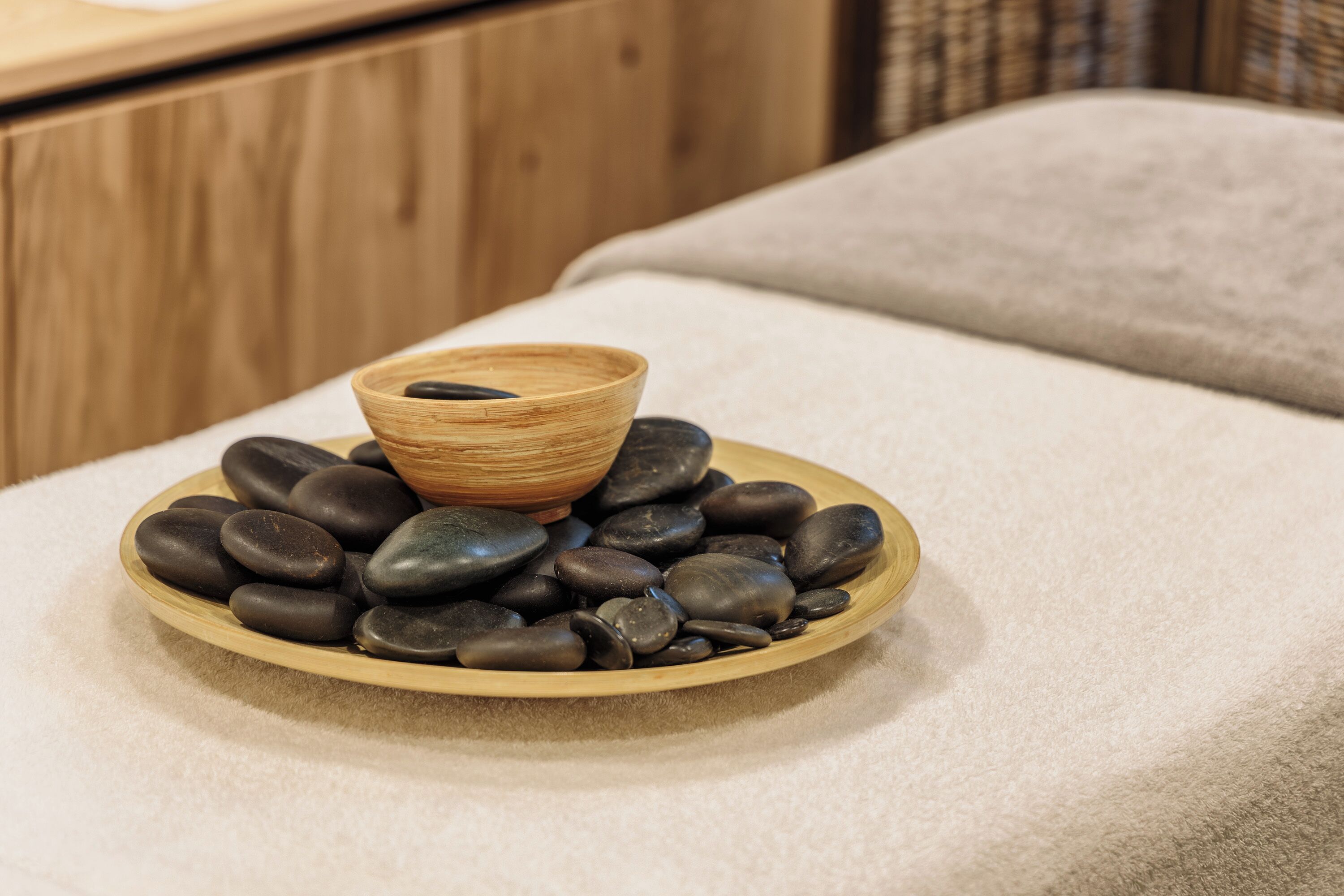 A wooden bowl with stones on a plate, placed on a white towel.