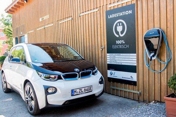 Un coche eléctrico blanco aparcado en una estación de carga, con un cartel que indica carga 100% eléctrica.