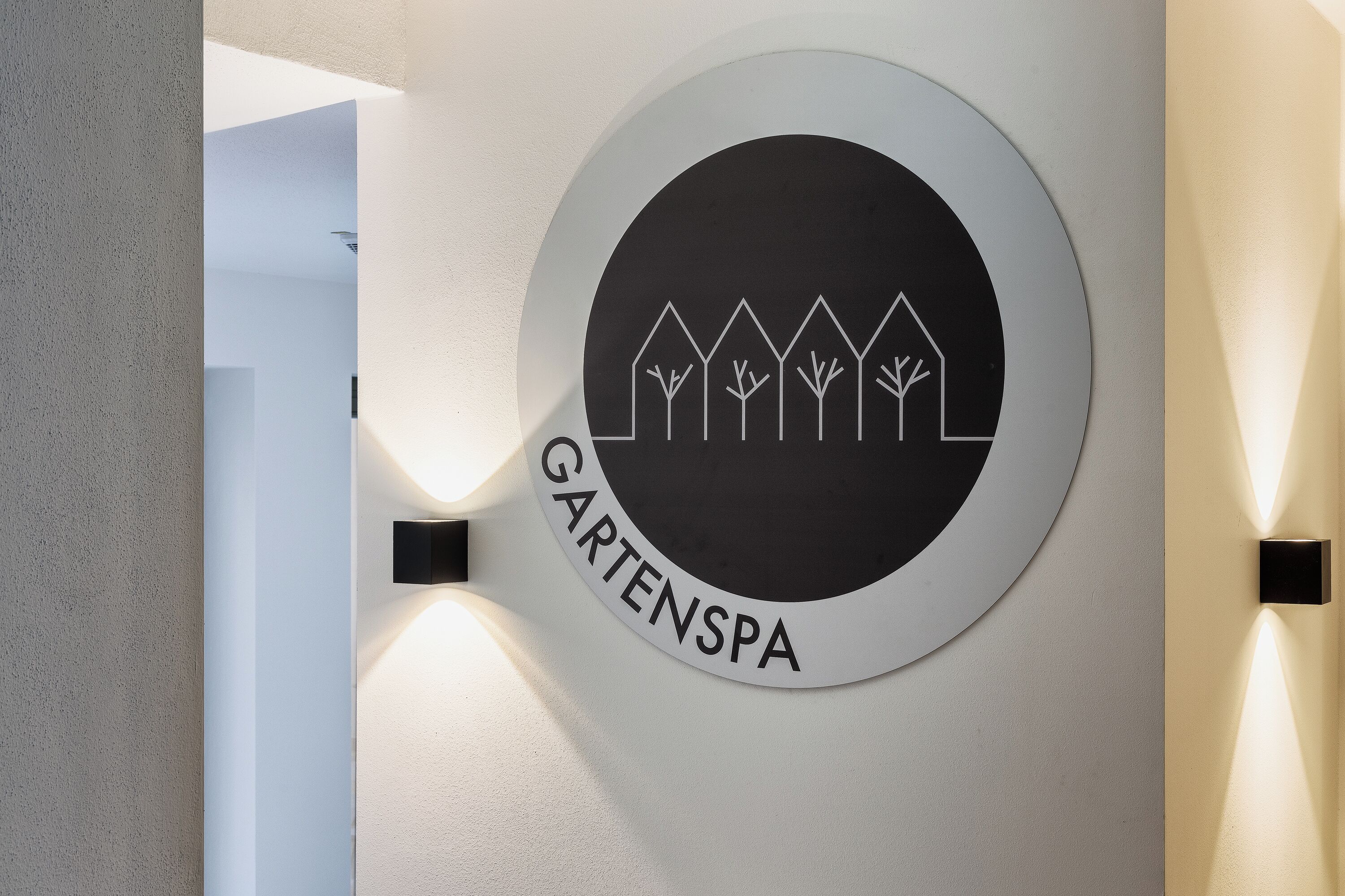 Una señal circular con un logo y el texto 'GARTENSPA' en una pared.