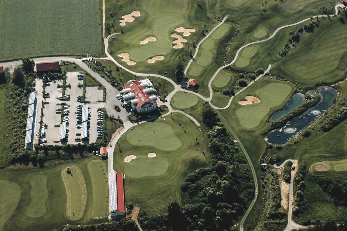 An aerial view of a golf course with bunkers, a clubhouse, and a parking lot.