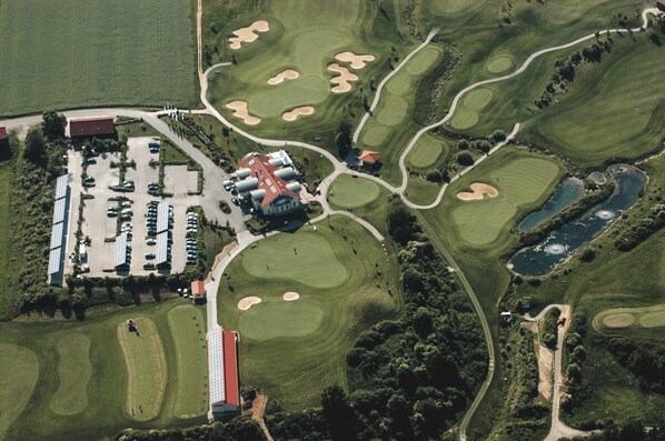 An aerial view of a golf course with bunkers, a clubhouse, and a parking lot. - Romantik Hotel Hirschen (Parsberg)