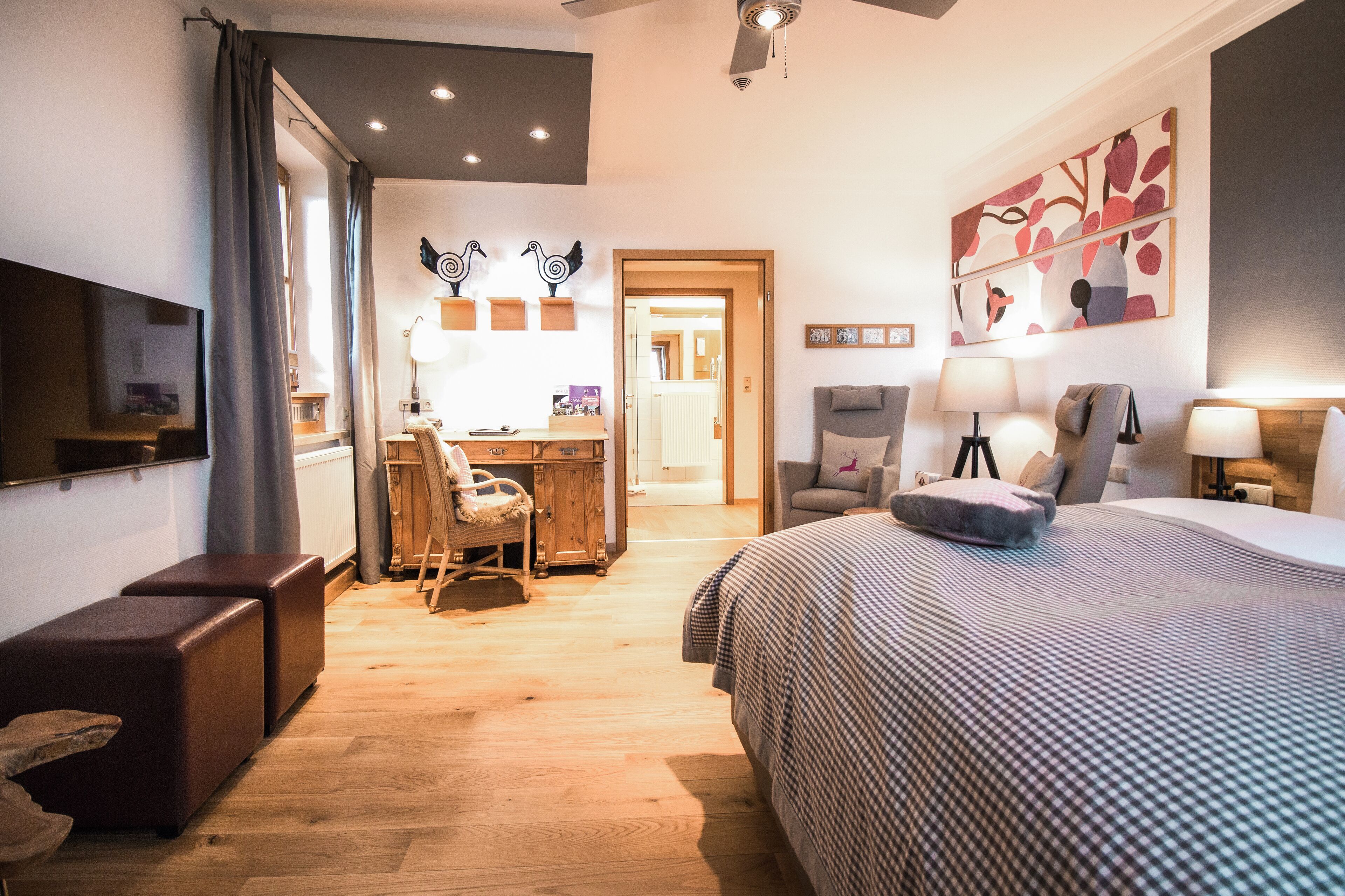 Ein Schlafzimmer mit einem großen Bett, einem Schreibtisch und einem Stuhl. Ein Fernseher ist an der Wand befestigt und es gibt einen Deckenventilator.