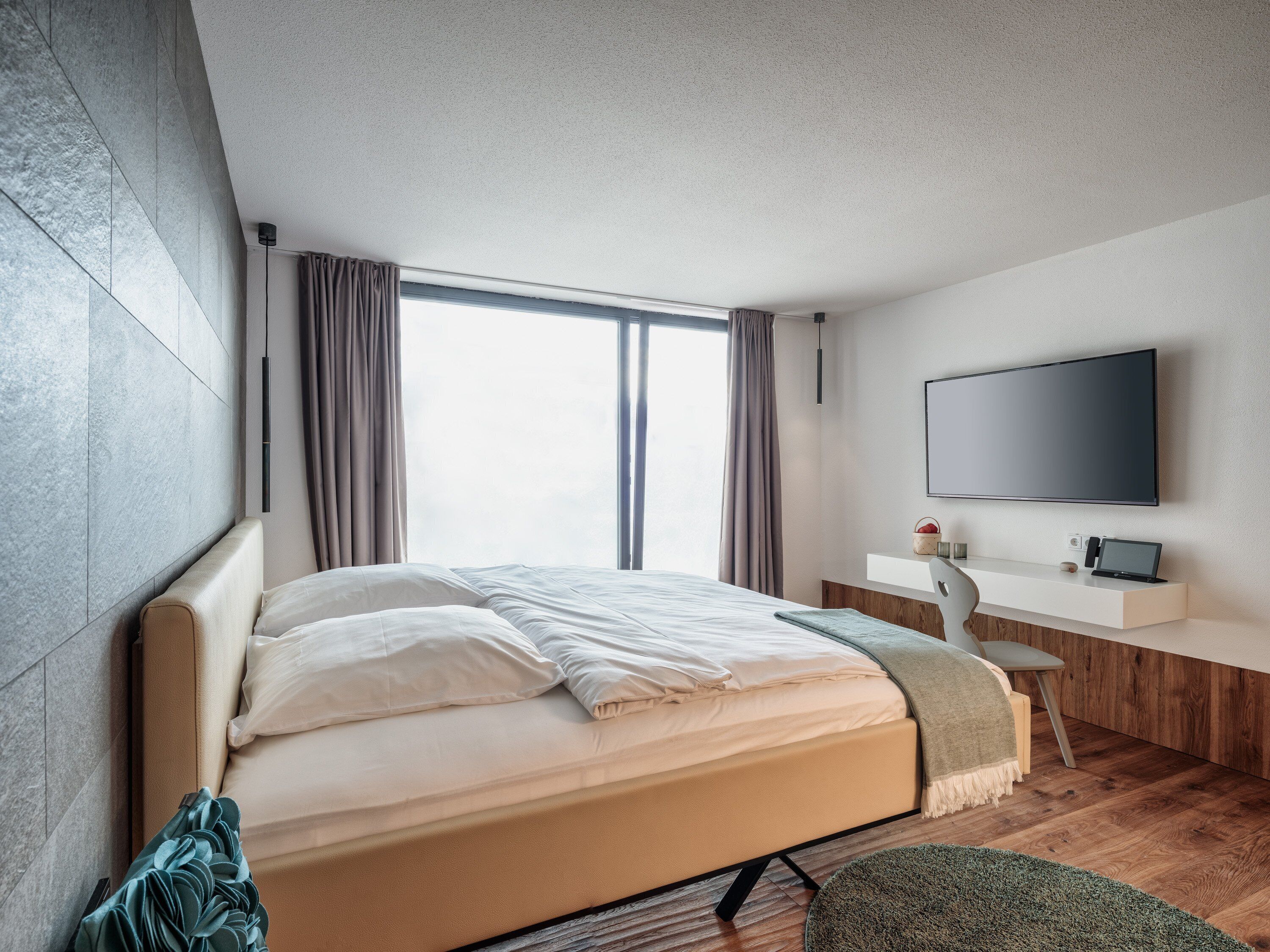 Un dormitorio moderno con una cama grande, un escritorio, un televisor de pantalla plana y un ventanal con cortinas.