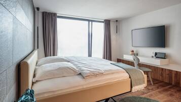 Un dormitorio moderno con una cama grande, un escritorio, un televisor de pantalla plana y un ventanal con cortinas.
