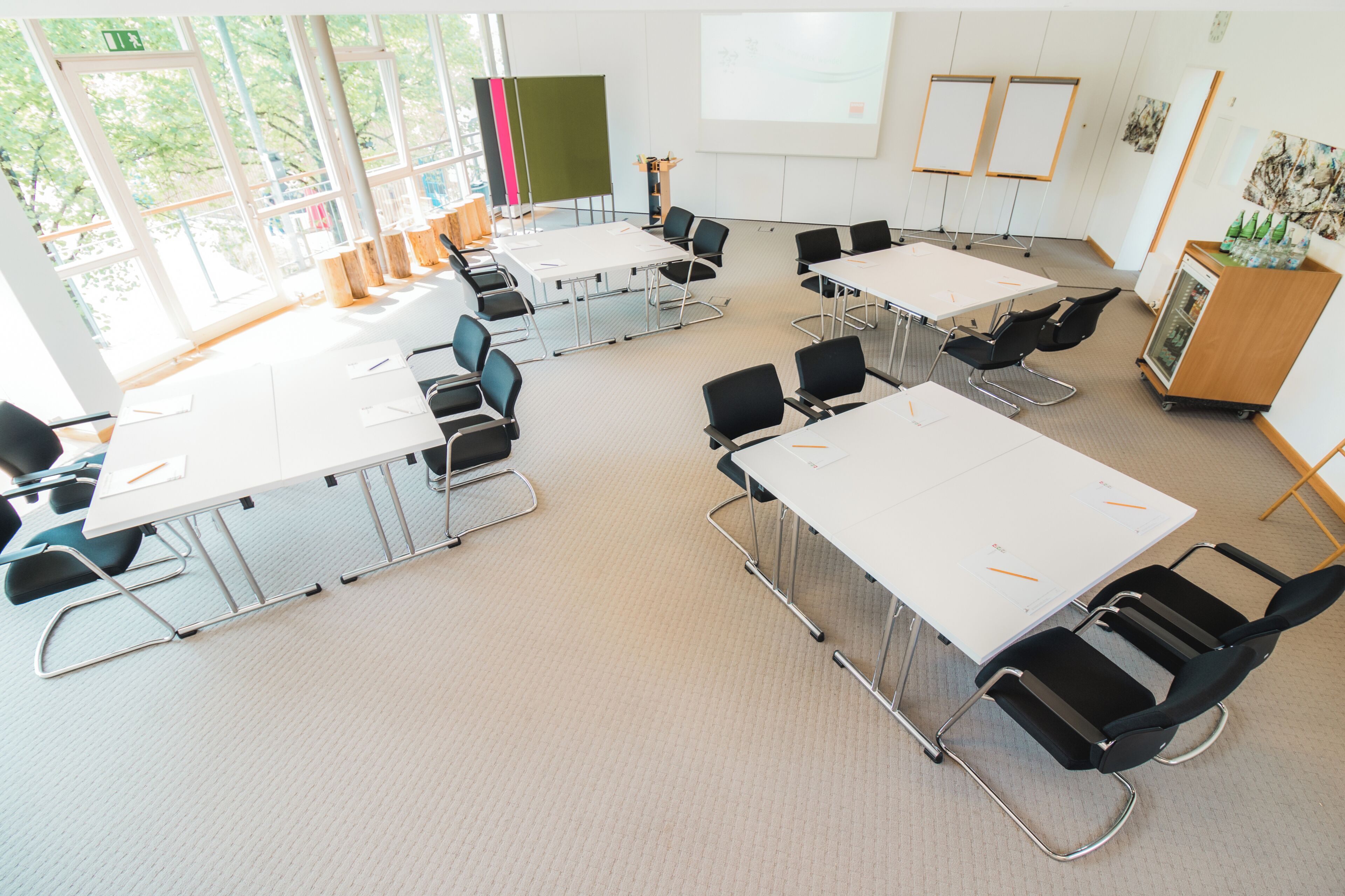 A conference room with tables, chairs, a whiteboard, and a projector screen.