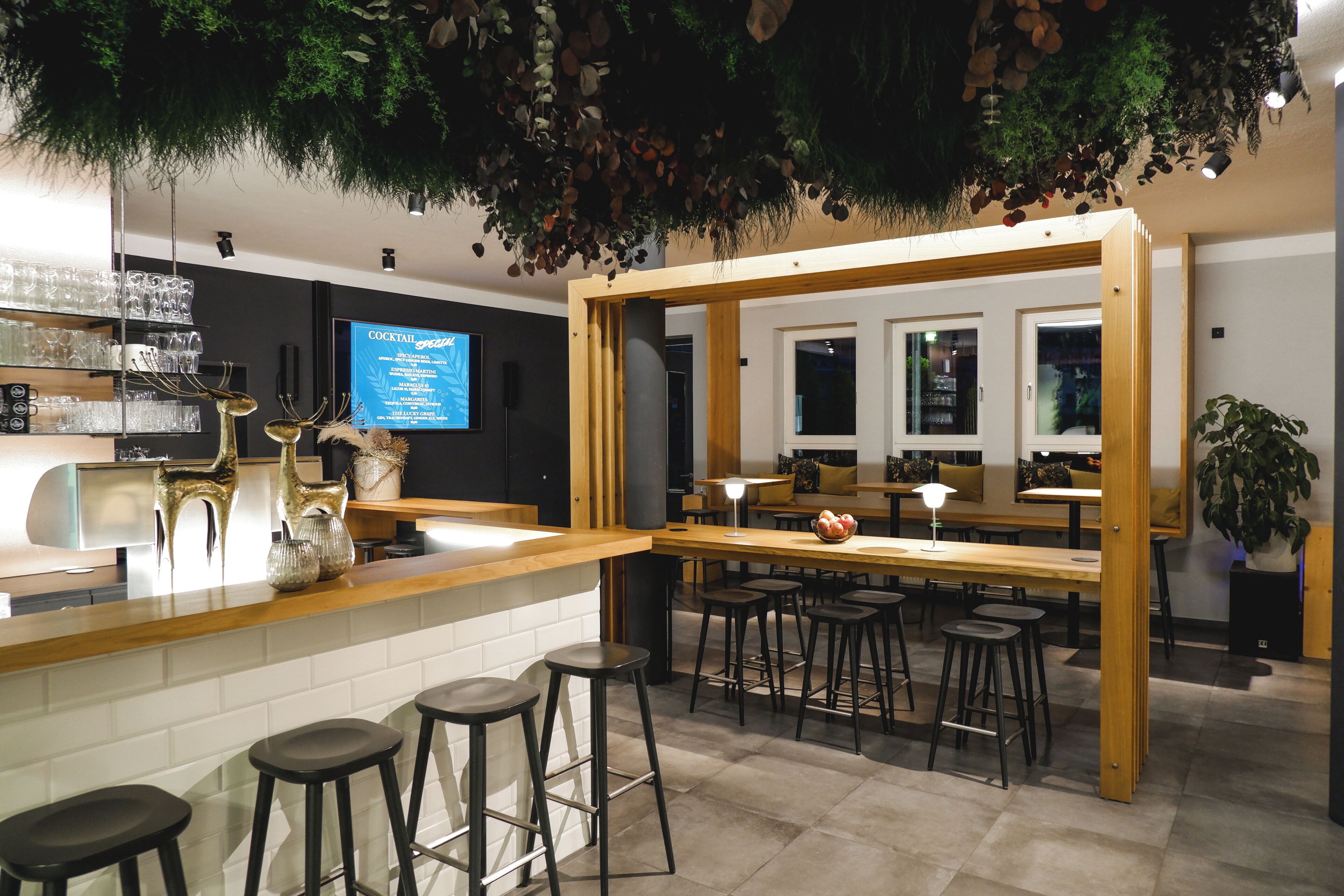 A bar area with stools, a counter with glasses, and a digital screen displaying a menu.