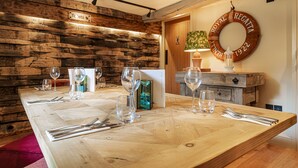 A wooden dining table set with wine glasses, cutlery, and a menu. A wooden wall with a 'Toilets' sign is visible, and a 'Royal Regatta 1922' sign hangs on the wall. - The George Hotel, Dorchester-on-Thames (Wallingford)