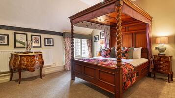 Een hemelbed met een bloemenbedekking, een houten nachtkastje met lades, en een tafel met een bloemig tafelkleed.