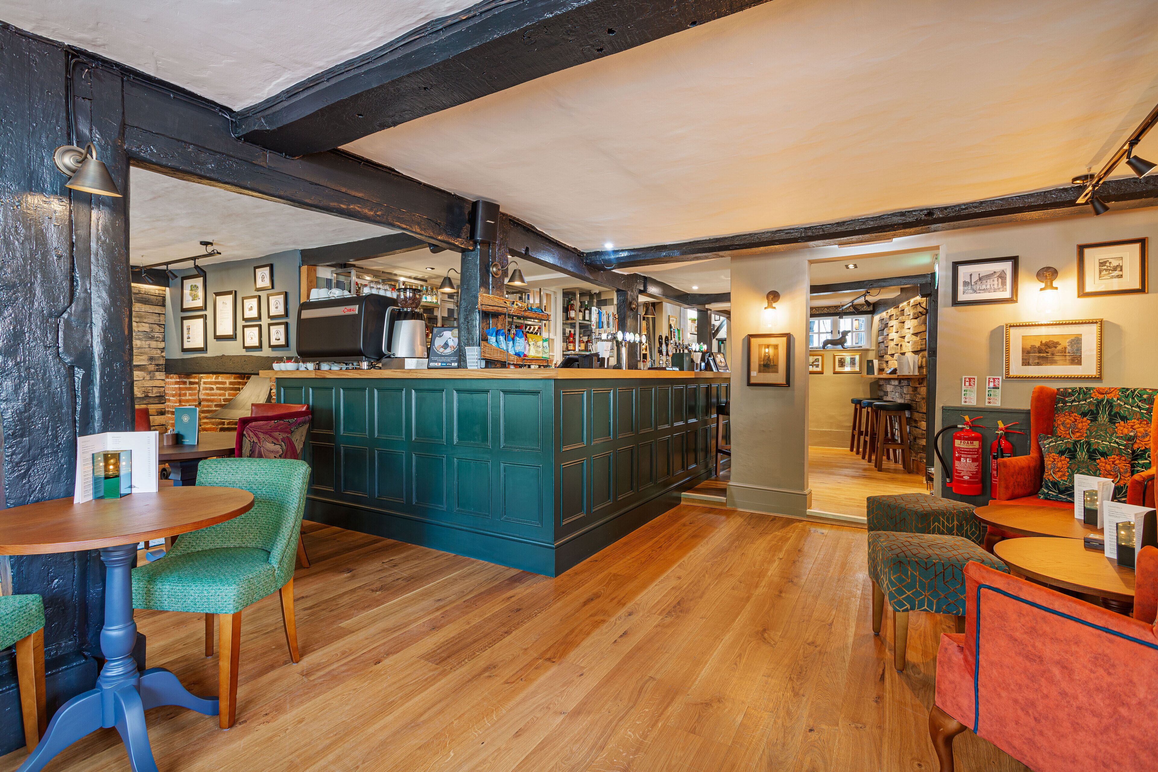 A bar area with wooden floors, green upholstered chairs, and a teal bar counter.