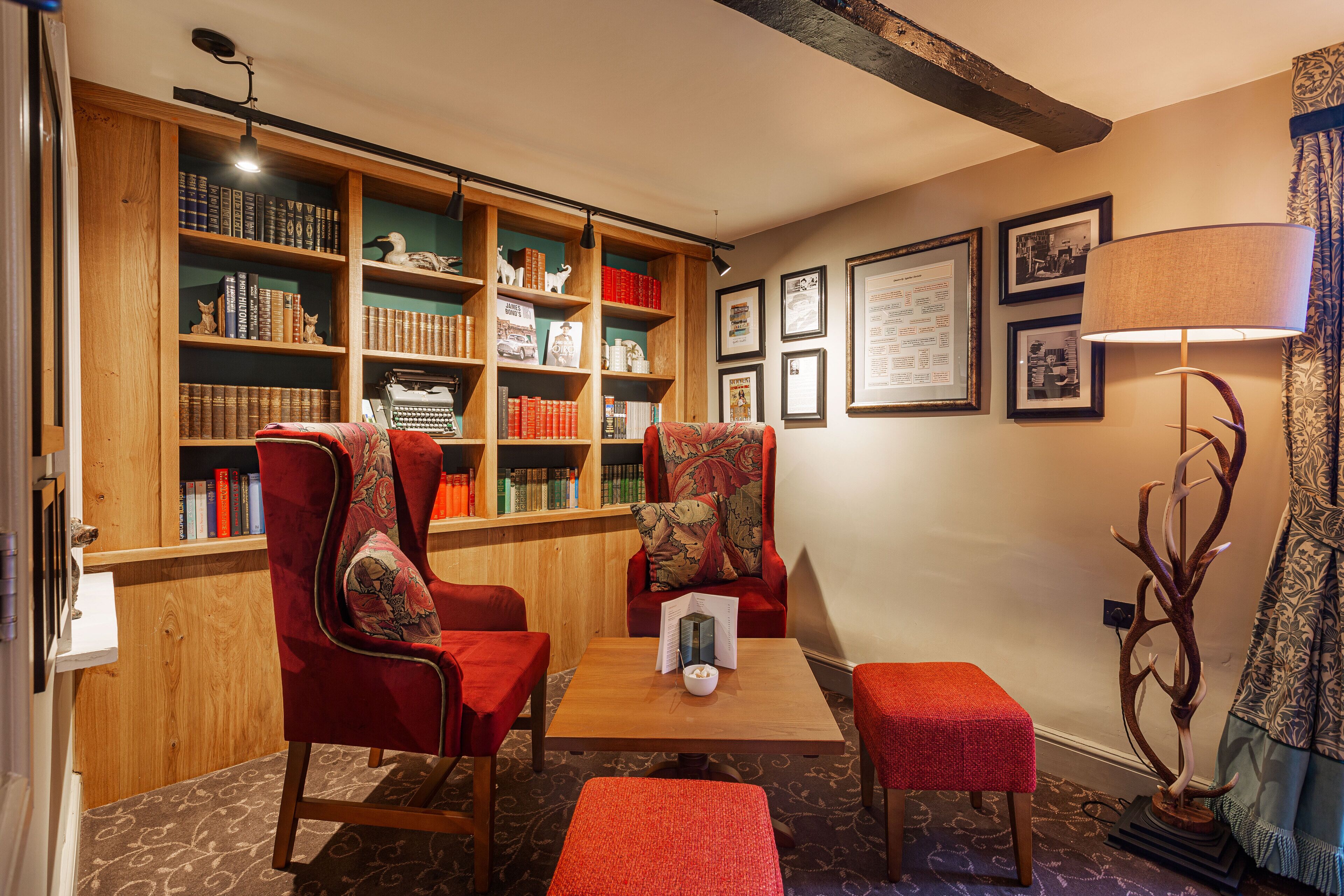 A cozy reading area with two red armchairs, a wooden table, and a bookshelf filled with books.