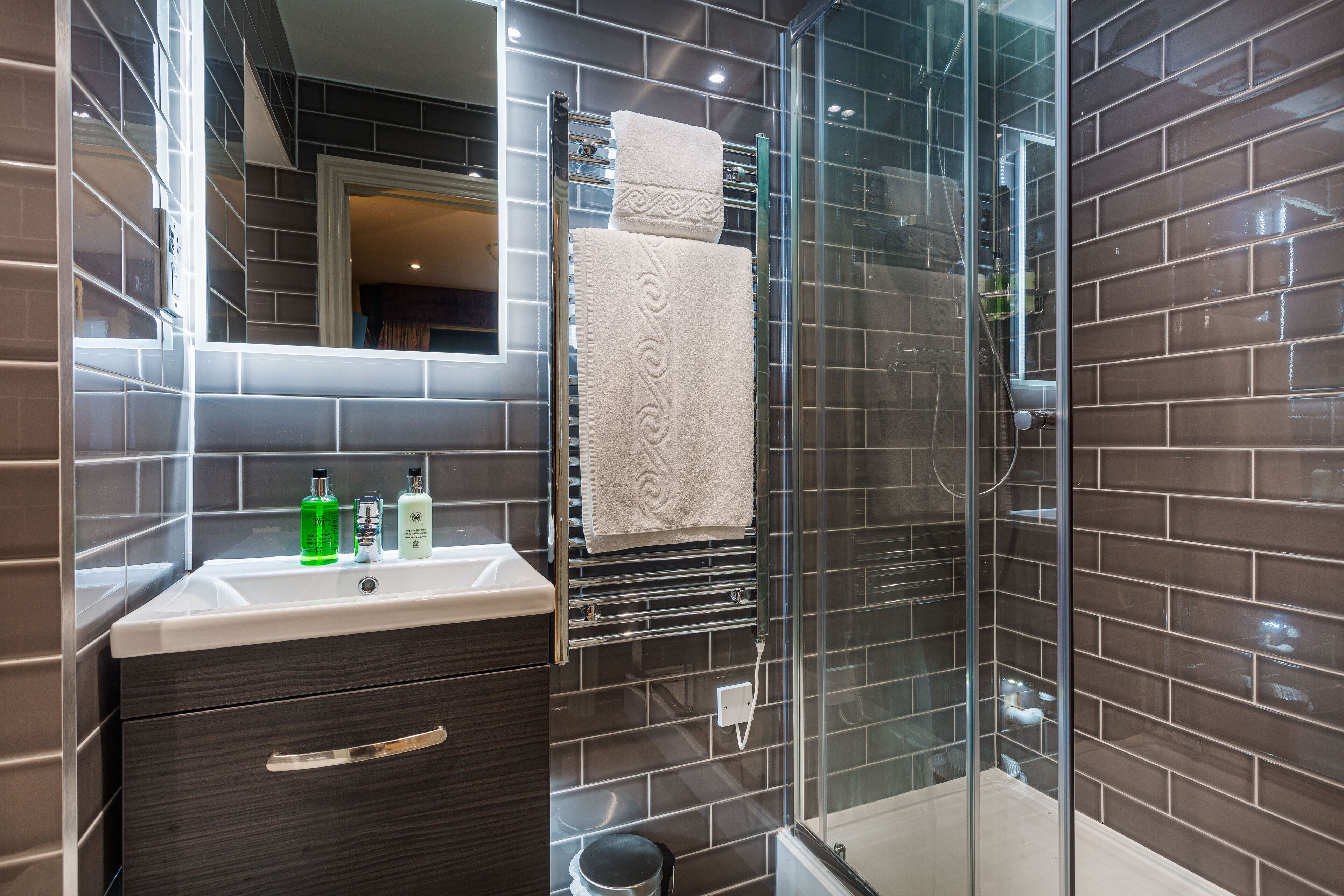Une salle de bain moderne avec une douche à parois de verre, un meuble-lavabo avec un miroir et un porte-serviettes.