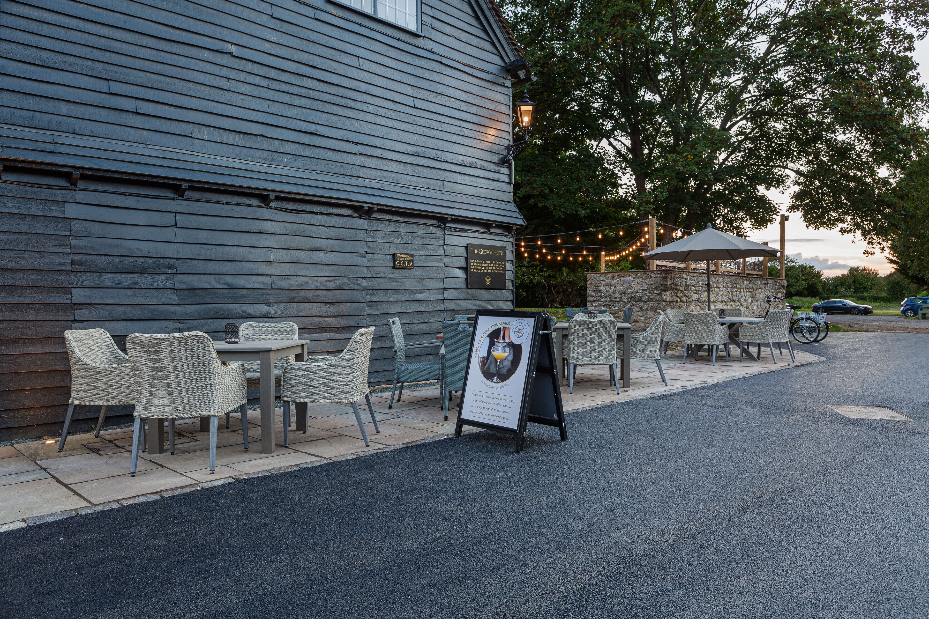 An outdoor seating area with wicker chairs and tables, a stone wall, and a signboard.