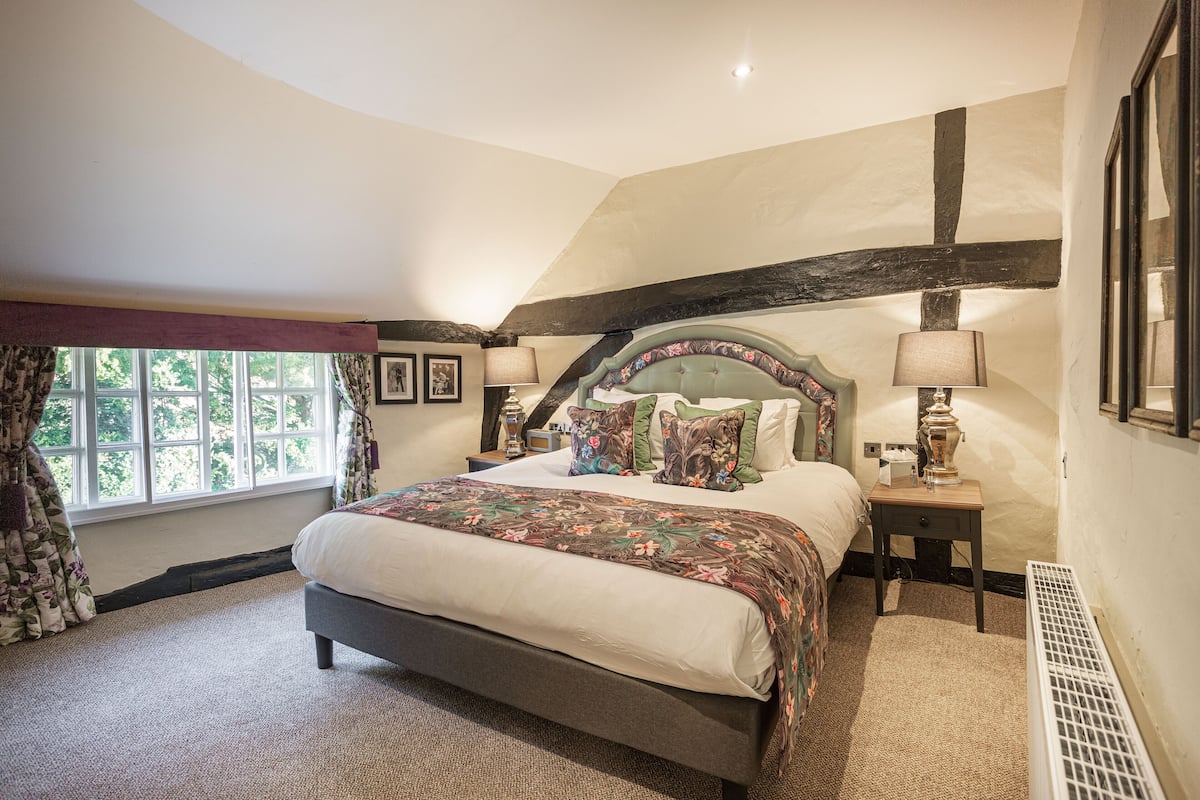 A bedroom with a large bed, a nightstand, a window with curtains, and a radiator.