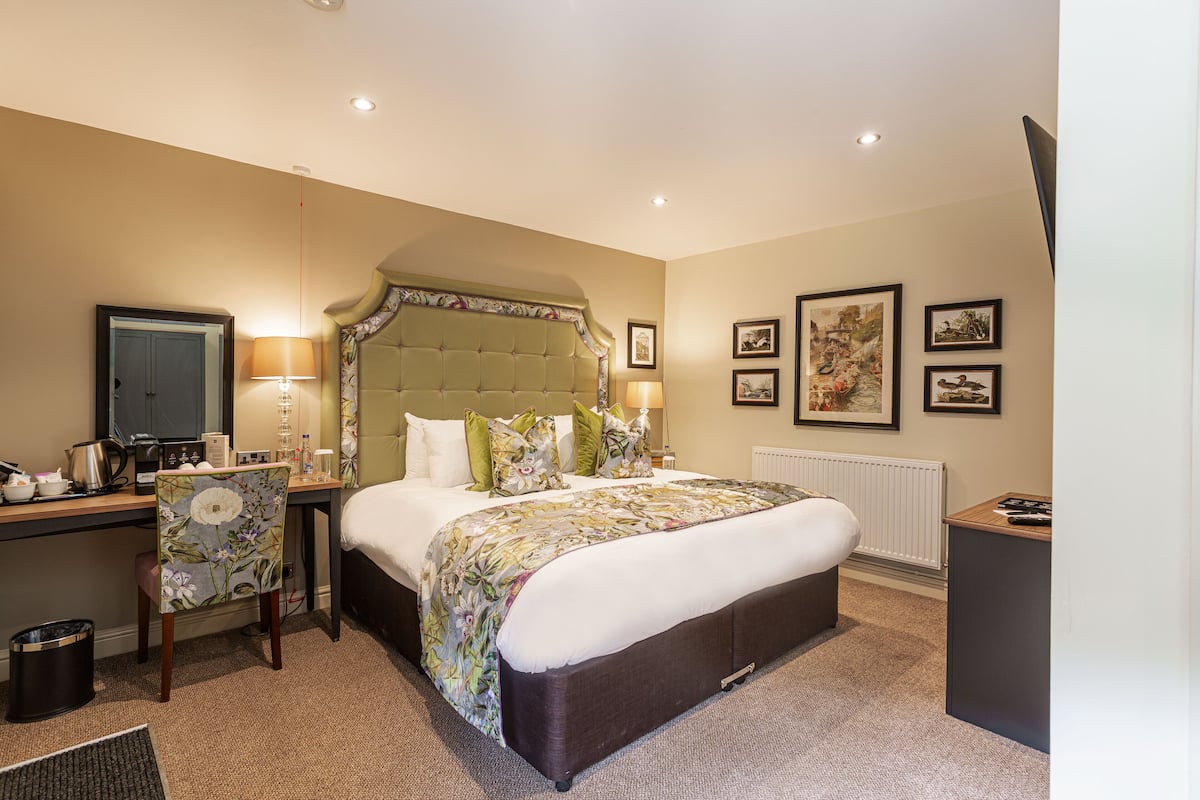 A hotel room with a large bed, a desk with a chair, a radiator, and framed pictures on the wall.
