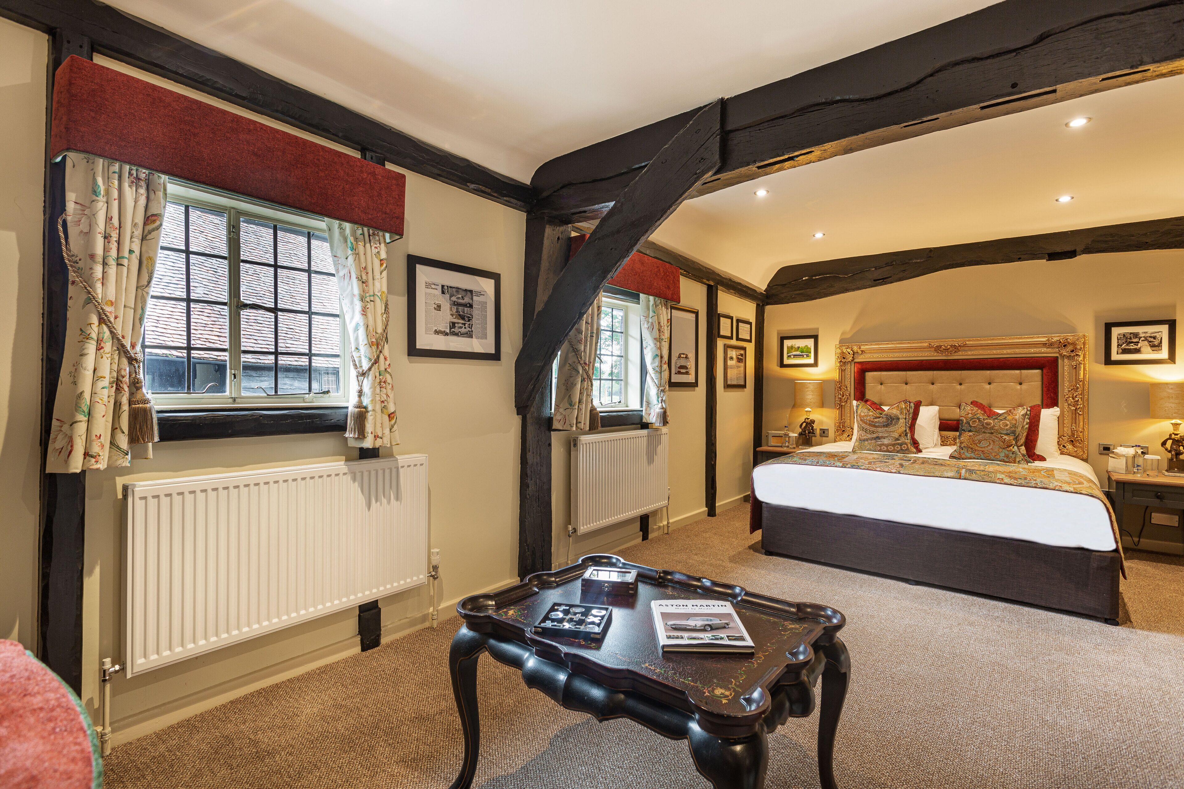 A bedroom with a large bed, a wooden table, and a window with curtains.