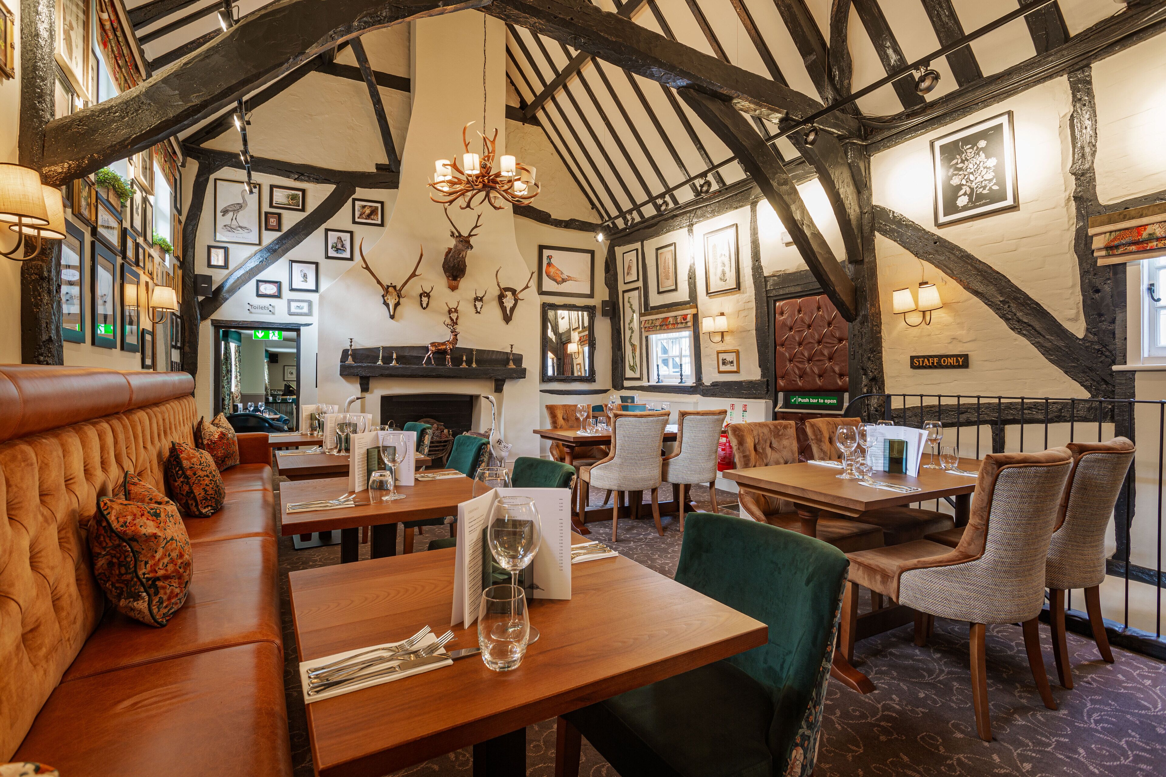 A restaurant with wooden tables, green upholstered chairs, and a high ceiling with exposed beams.