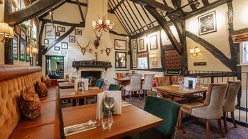 A restaurant with wooden tables, green upholstered chairs, and a high ceiling with exposed beams.