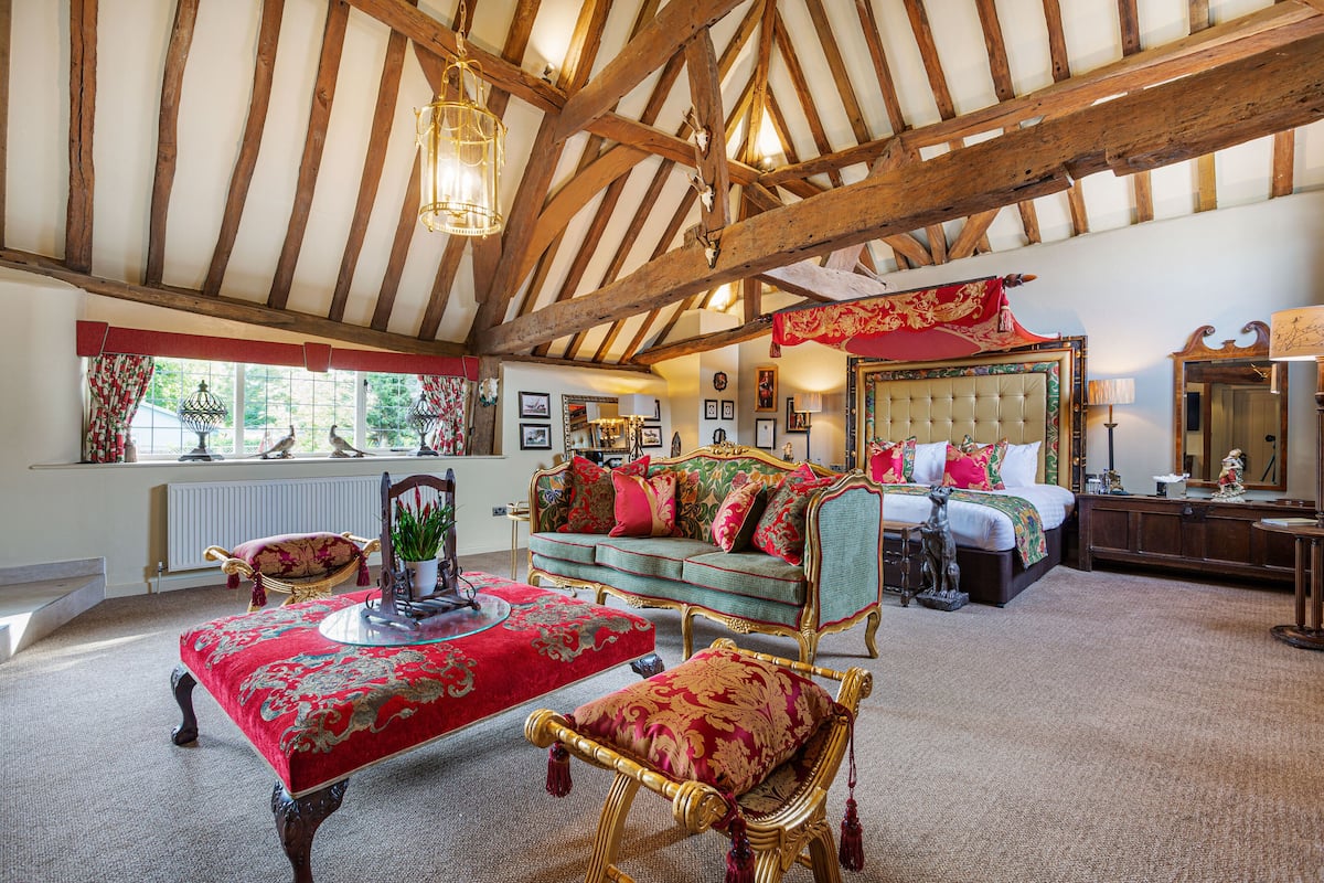 A traditional room with a high ceiling, a bed with ornate headboard, a red and gold patterned sofa, and a wooden floor.