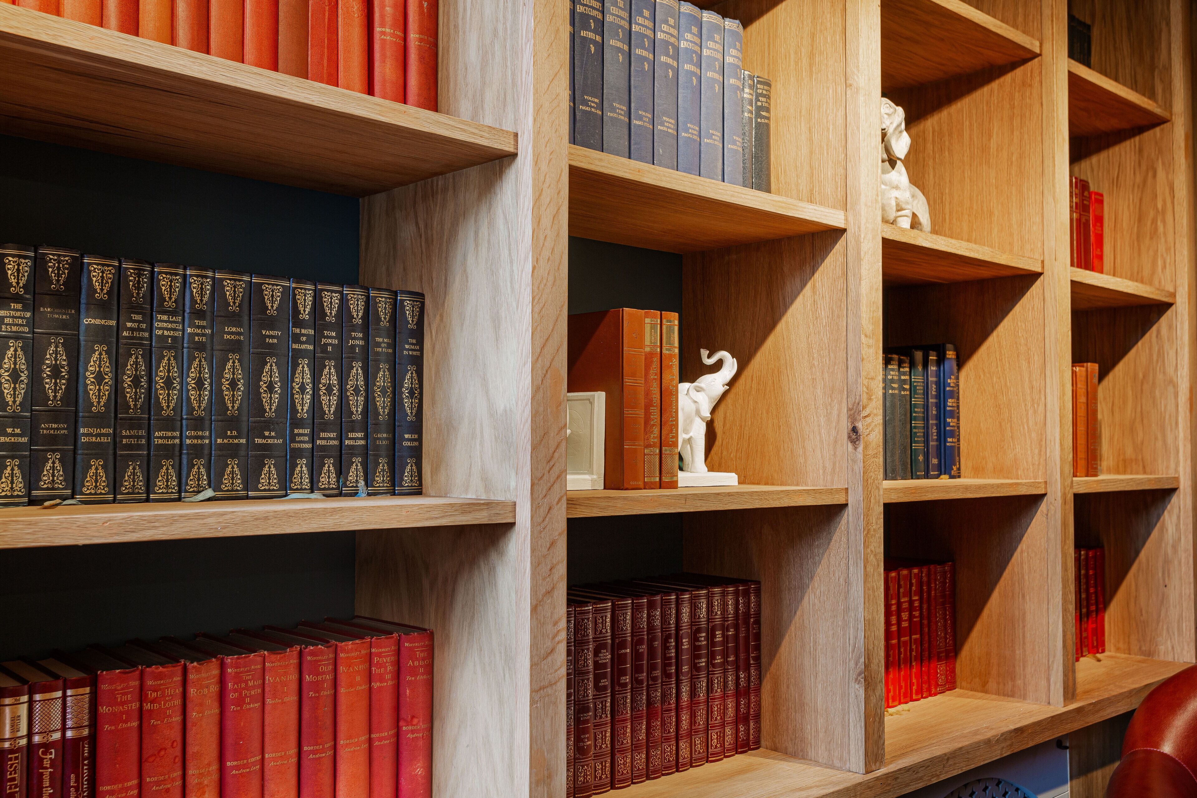 Una libreria con diversi libri, una statua bianca e una sedia rossa.
