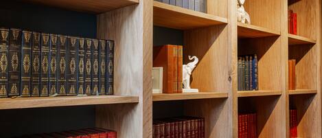 Una libreria con diversi libri, una statua bianca e una sedia rossa.
