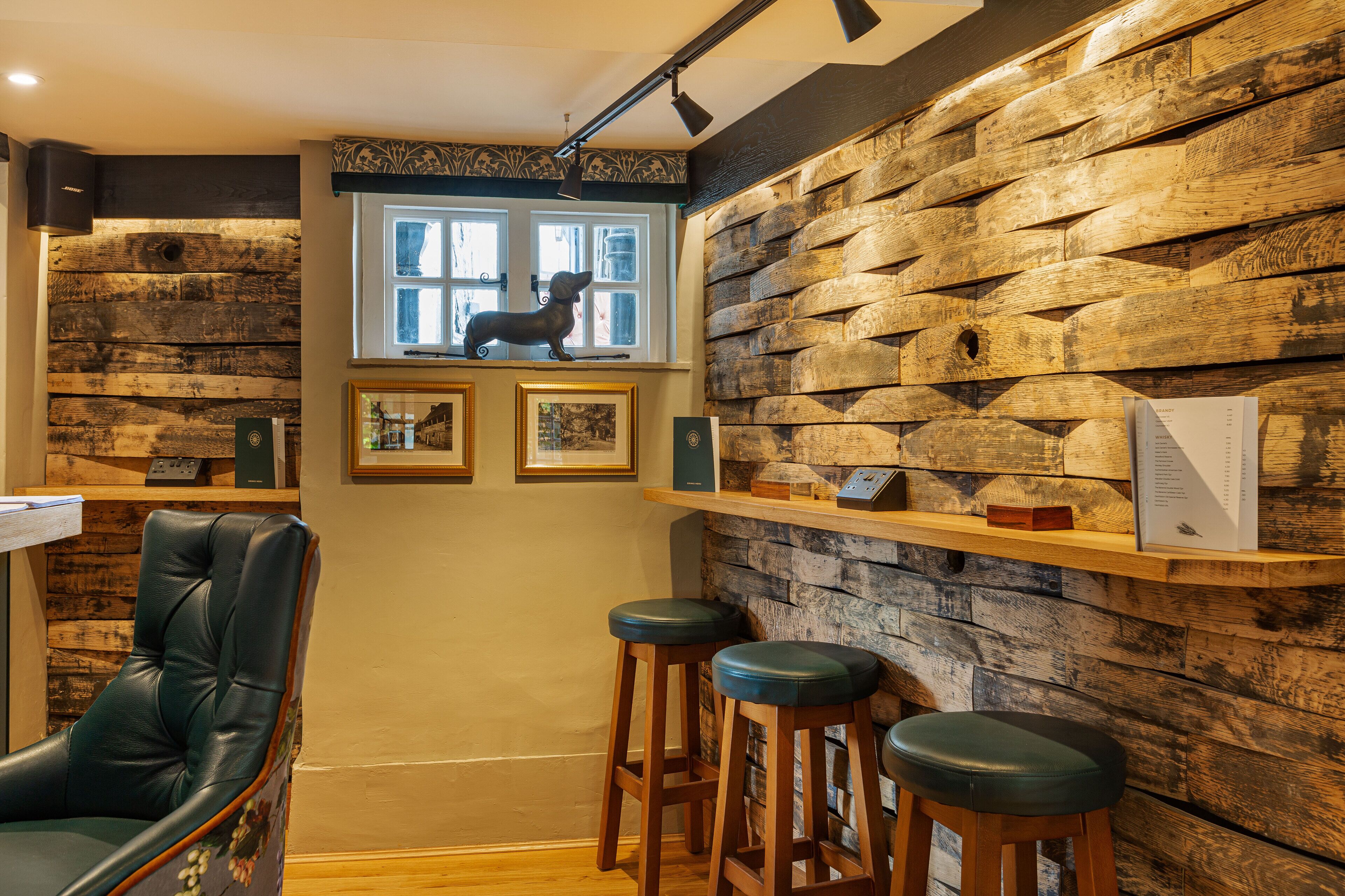 Een rustiek interieur met een houten wand, een raam met een beeld van een hond, ingelijste foto's en een bar met krukken.