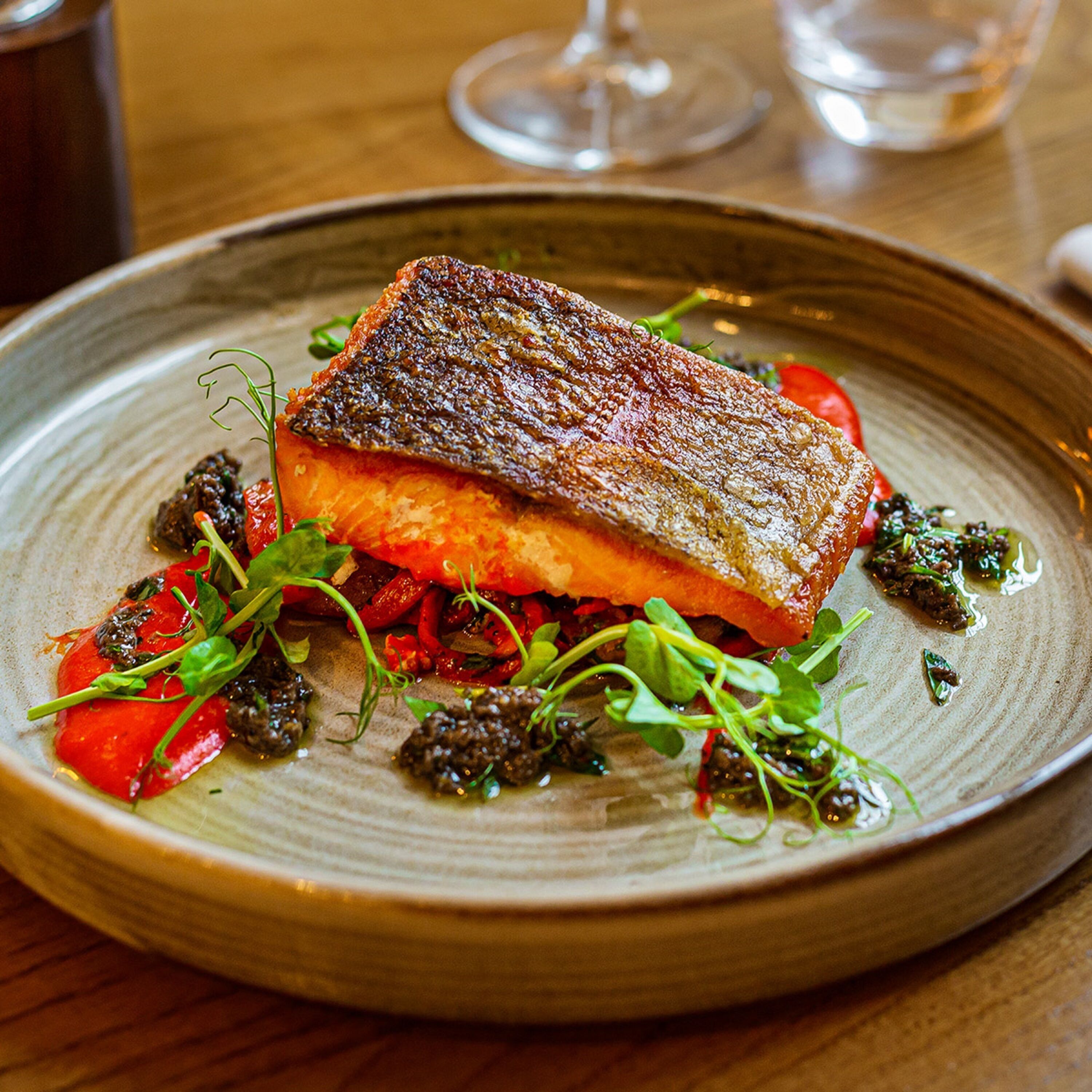 A plate of food with a piece of fish, vegetables, and greens.