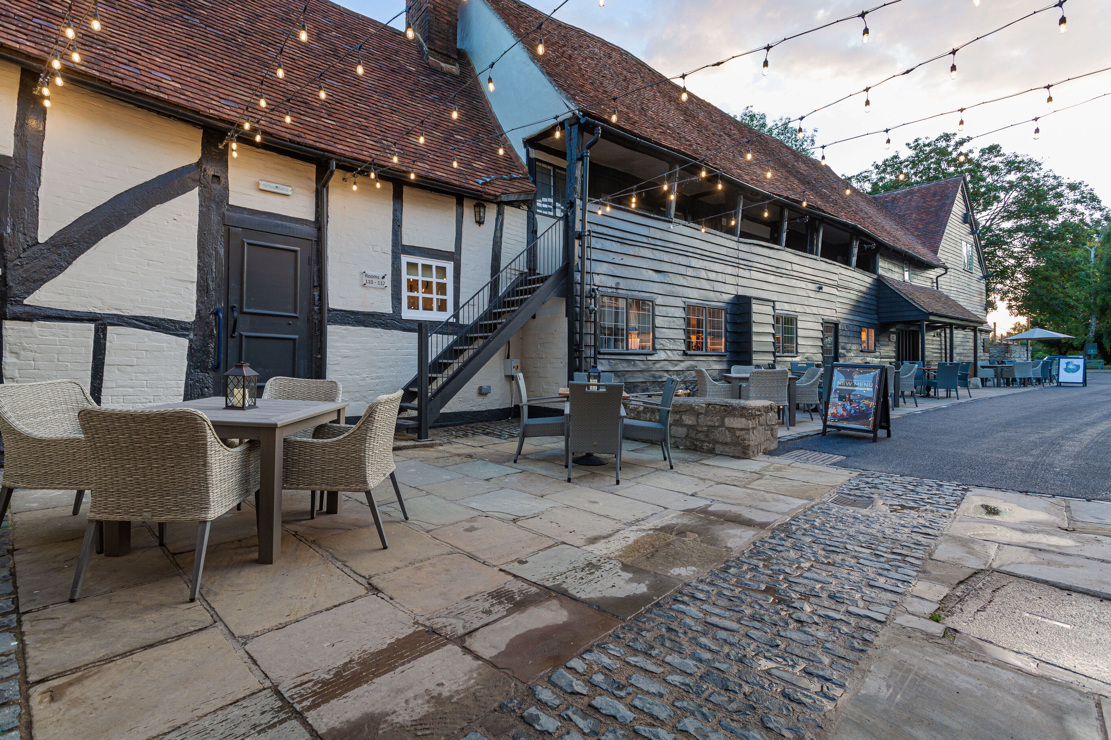 An outdoor seating area with wicker chairs and a table, a staircase leading to the building, and string lights above.