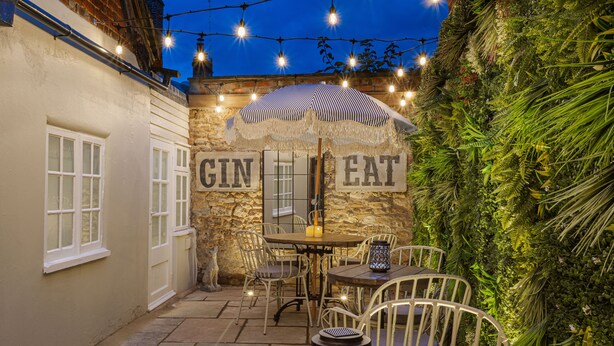 An outdoor patio with a stone wall, a table and chairs, an umbrella, and string lights.