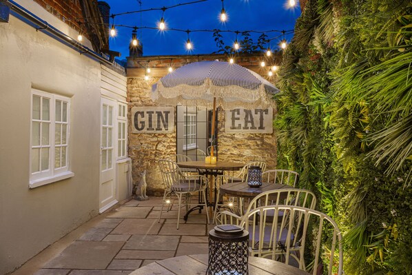 An outdoor patio with a stone wall, a table and chairs, an umbrella, and string lights.