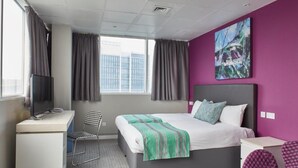 Una habitación de hotel moderna con cama, escritorio, silla y un ventanal grande.