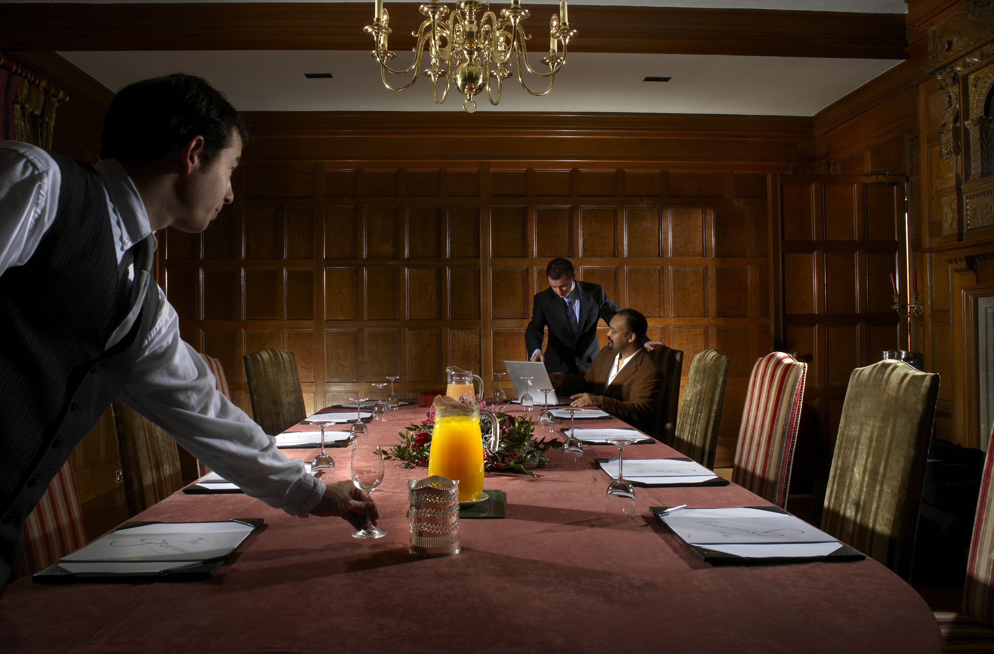 A conference room with a long table, wooden paneling, and a chandelier.