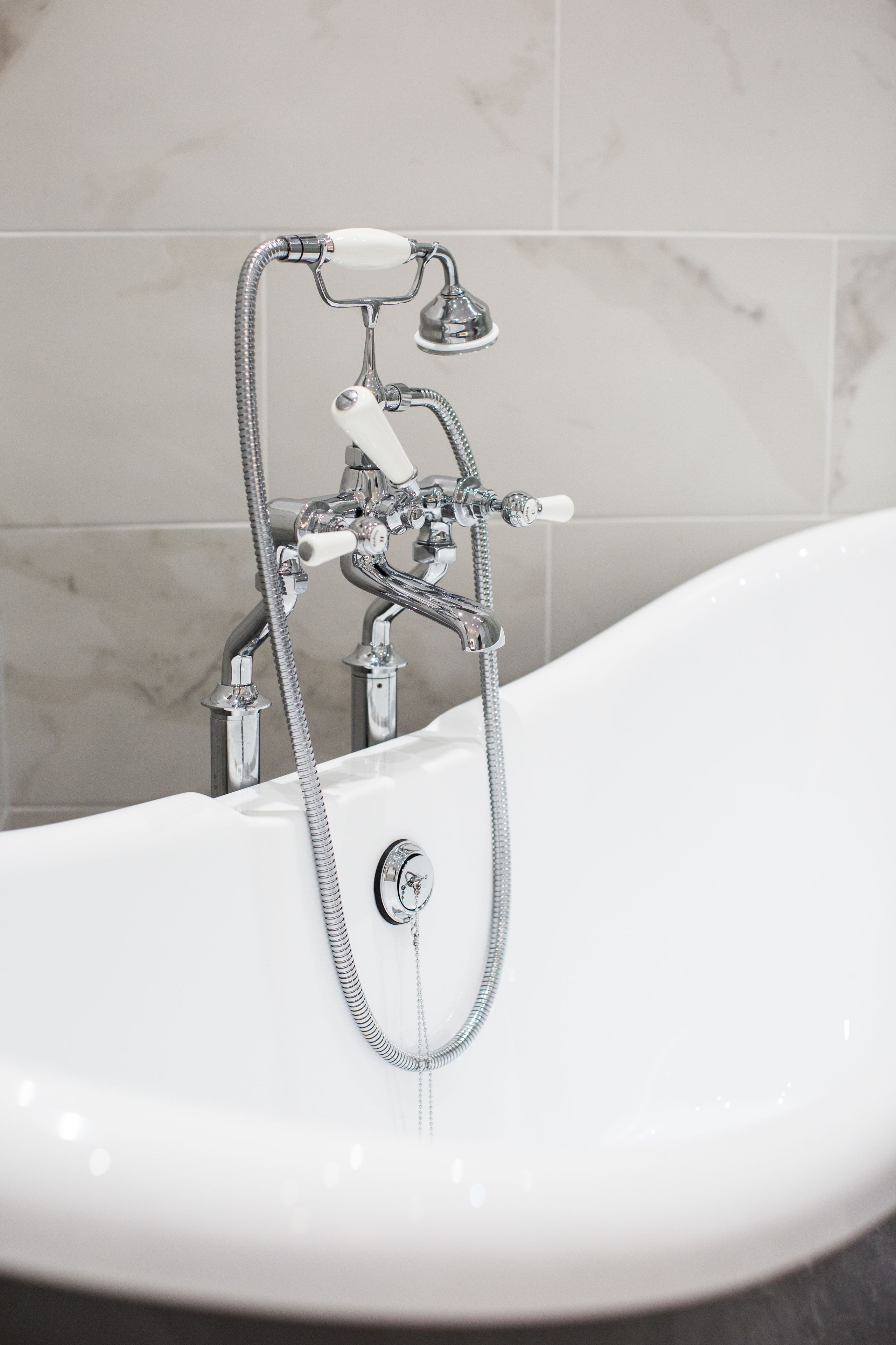 Une salle de bain moderne avec une baignoire sur pieds, des accessoires chromés et un mur recouvert de carreaux de marbre.