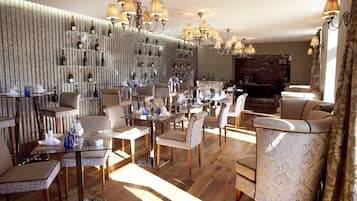 A dining area with glass tables and chairs, a wine rack with bottles, and a brick wall in the background.