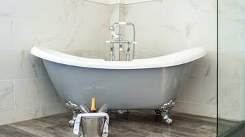 A modern bathroom with a freestanding bathtub, marble tiles, and a wooden floor.