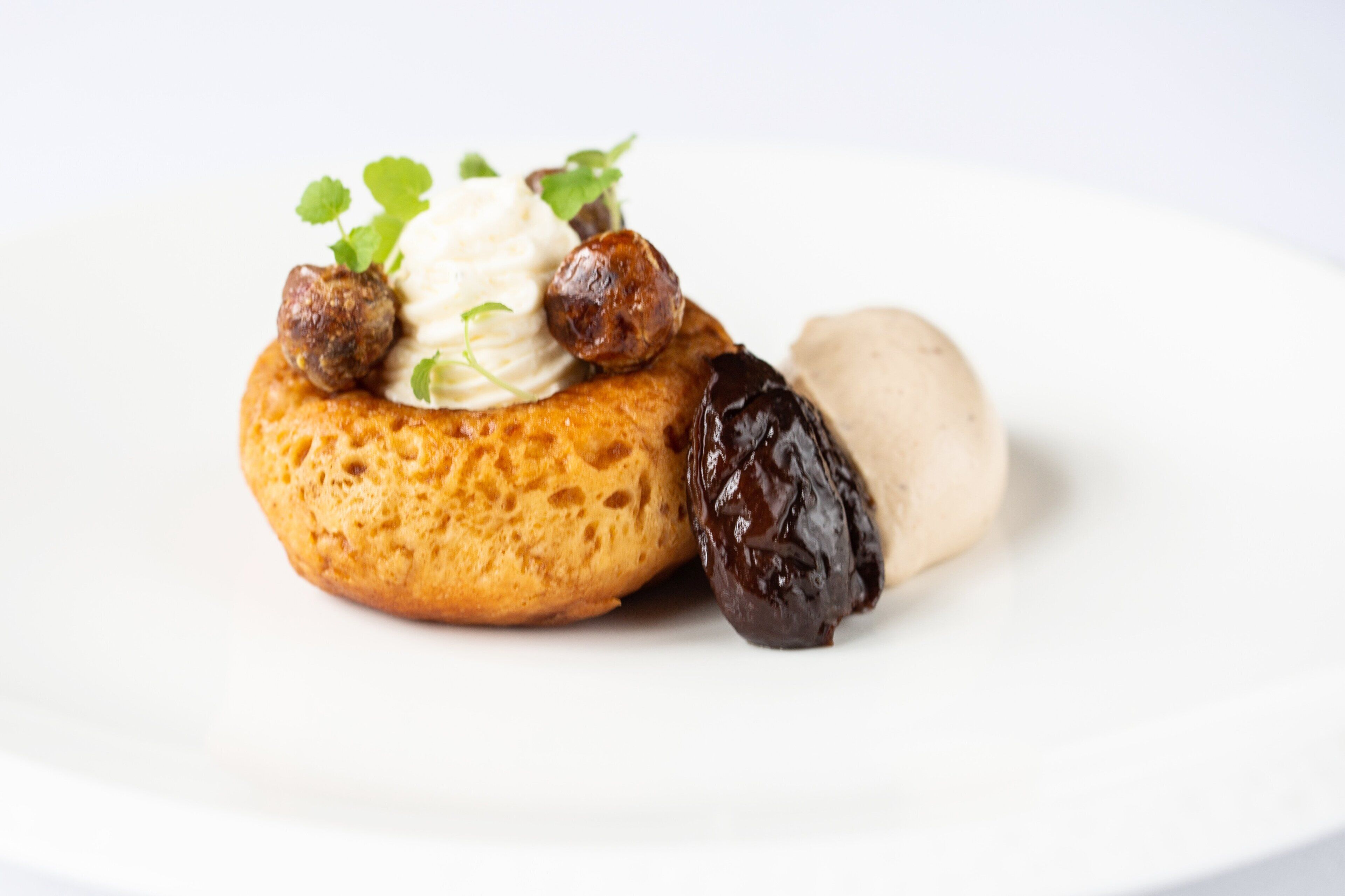 Un postre con base de hojaldre, cucharadas de crema y una fruta oscura sobre un plato blanco.
