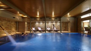 Piscina interna com teto de madeira, paredes de pedra e vista para o exterior.