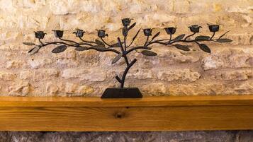 A metal sculpture of a tree with leaves and flowers on a wooden shelf against a stone wall.