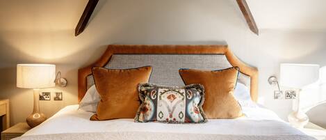 A hotel room with a large bed, two pillows, a nightstand with a lamp, and a wall-mounted light.