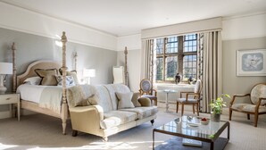 Quarto com cama de dossel, sofá, mesa de centro e vista do jardim através de uma janela ampla.