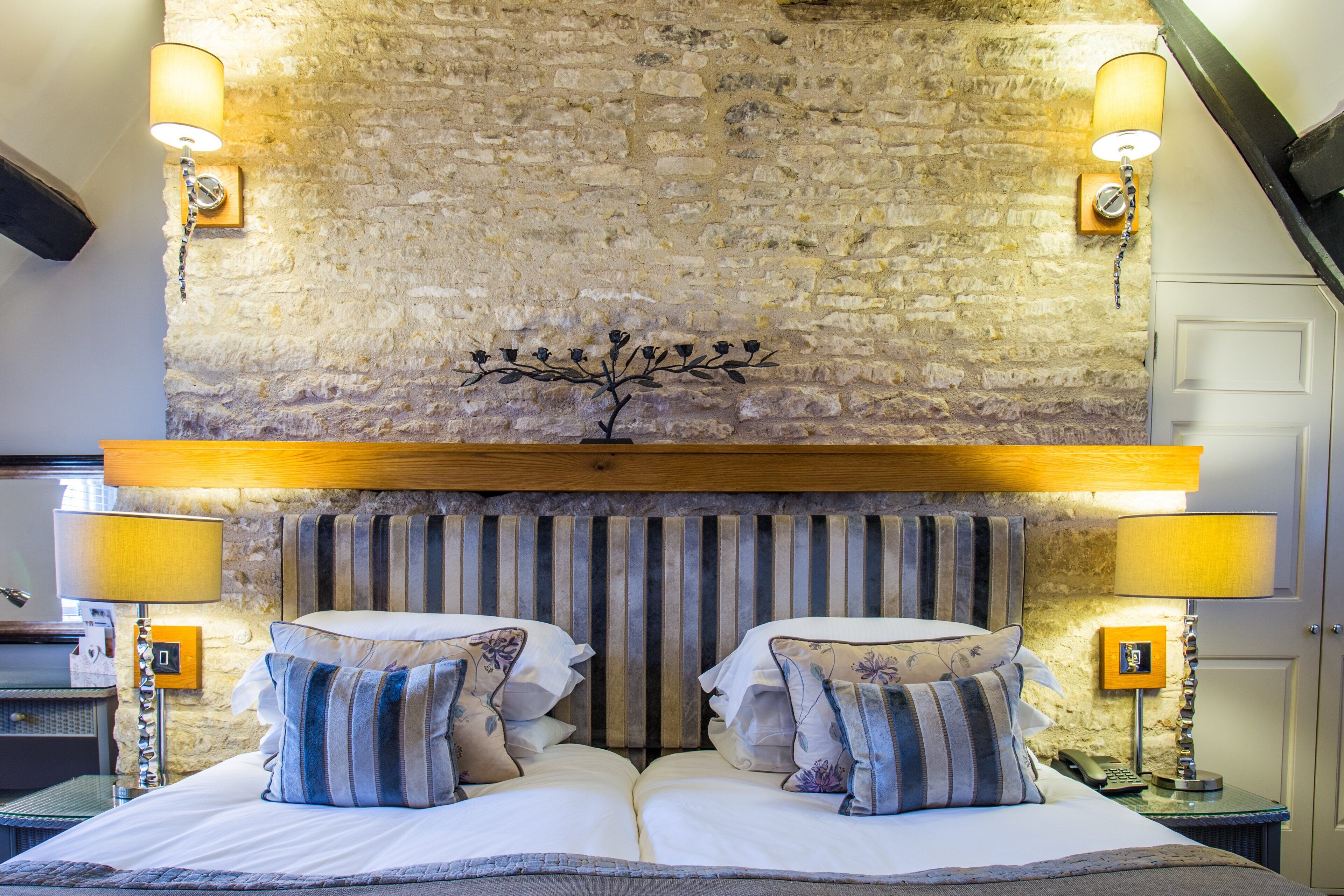 Ein Schlafzimmer mit einer Steinswand, einem hölzernen Kopfteil und zwei Nachttischlampen.