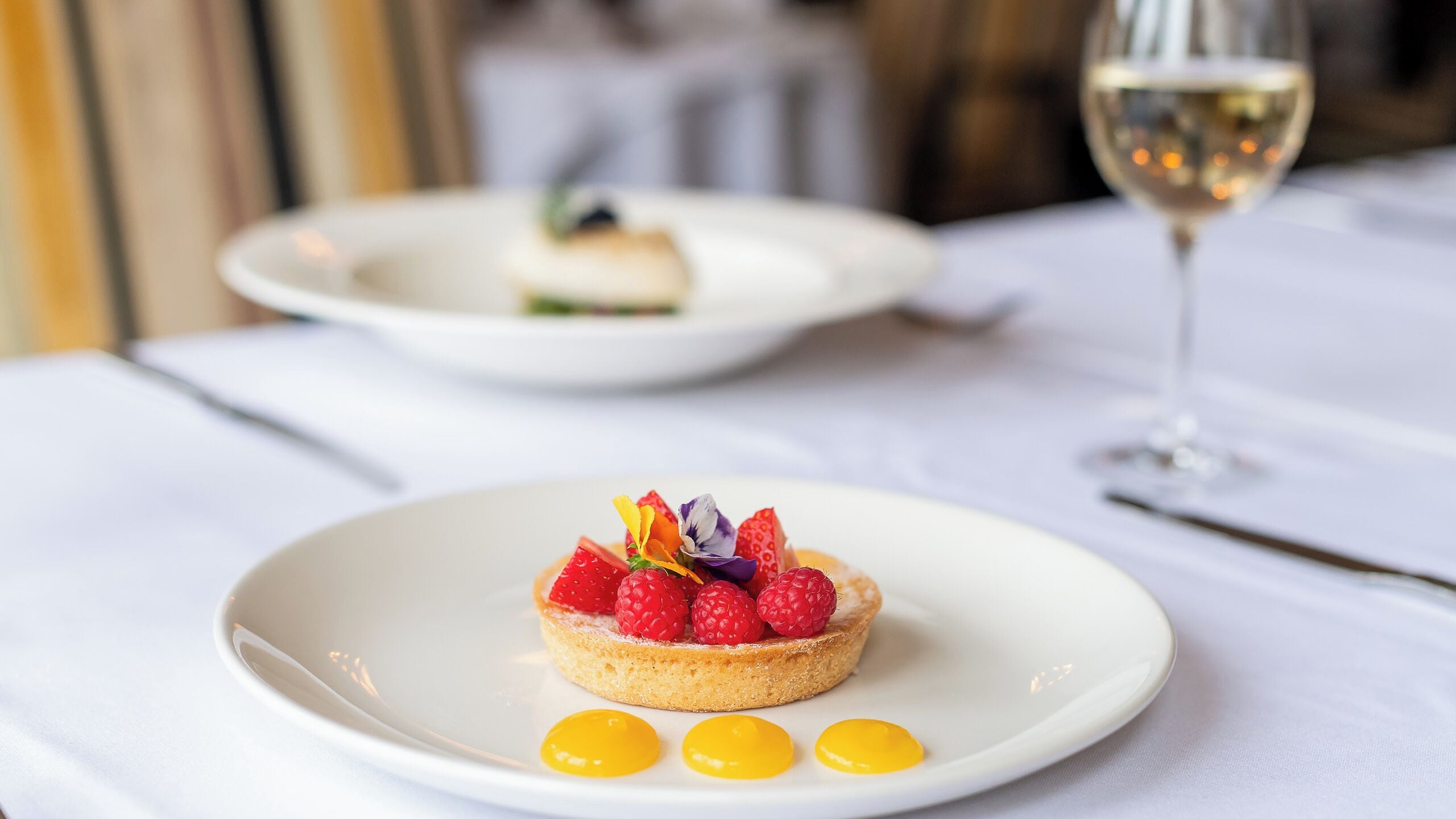 A dessert on a white plate with a glass of white wine in the background.