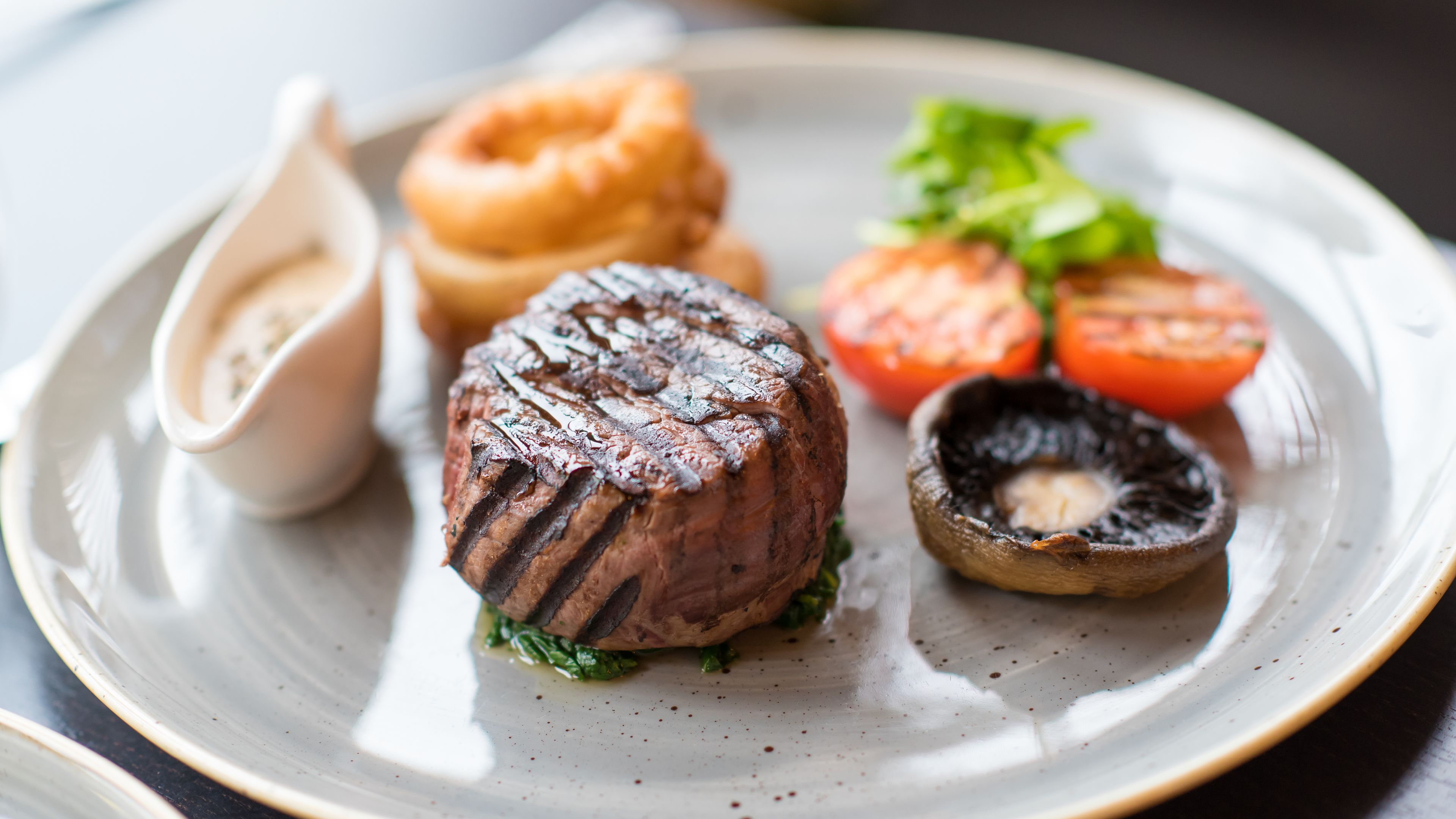 A plate with grilled steak, grilled tomatoes, grilled mushrooms, and onion rings.