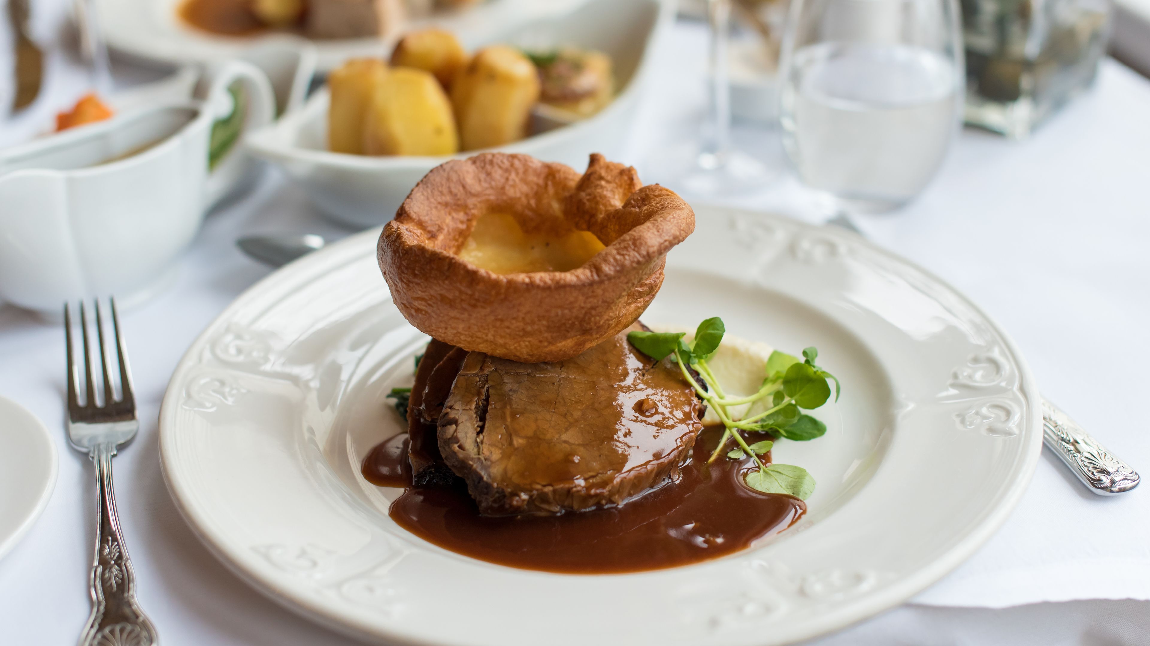 A plate with a Yorkshire pudding, meat, and sauce, accompanied by a fork and a decorative spoon.