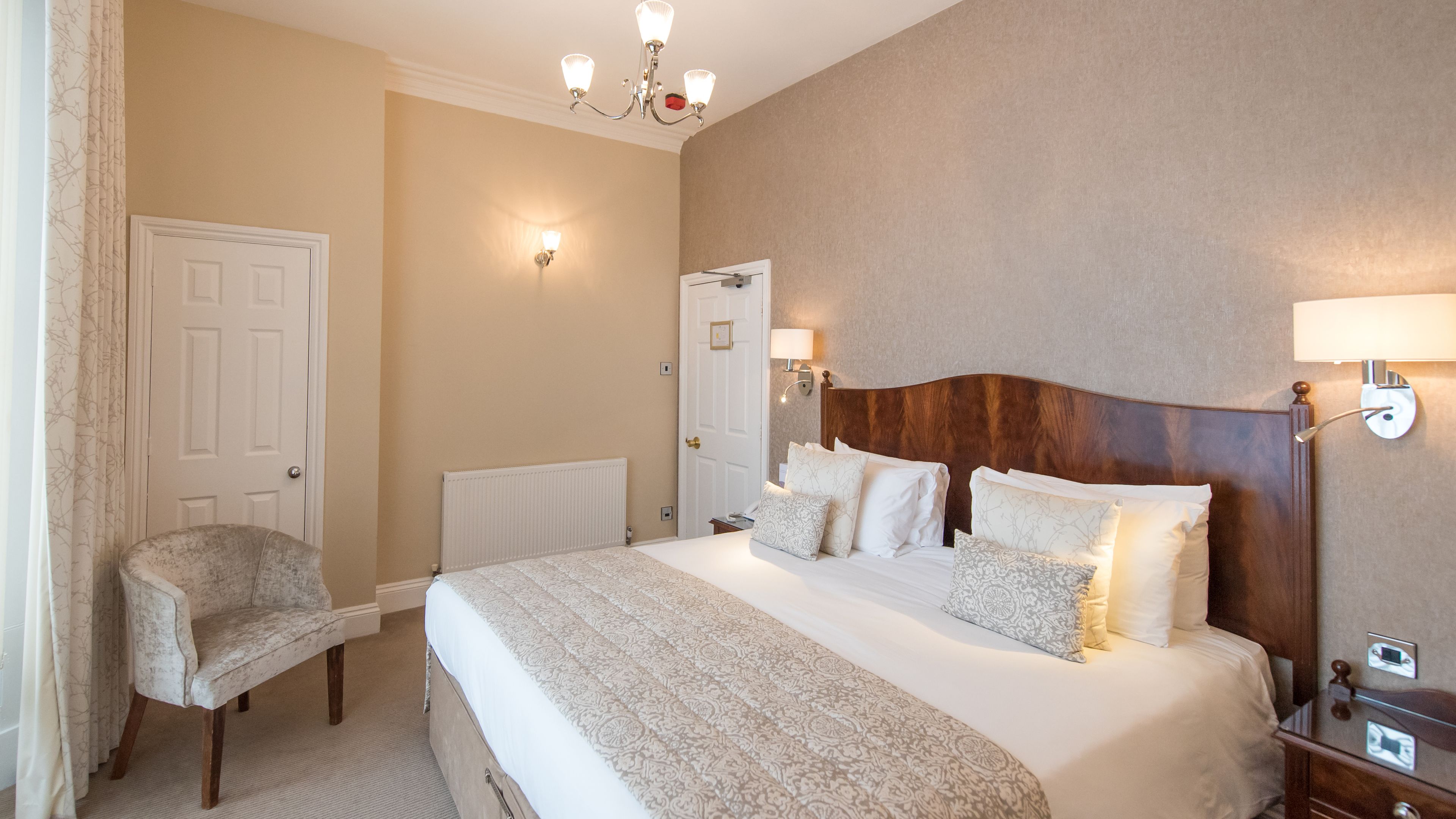 A hotel room with a large bed, a chair, a nightstand, and a wall-mounted lamp.