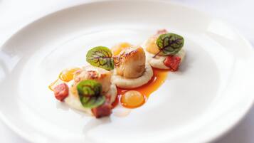 A white plate with a seared scallop, a dollop of sauce, and a garnish of green leaves.