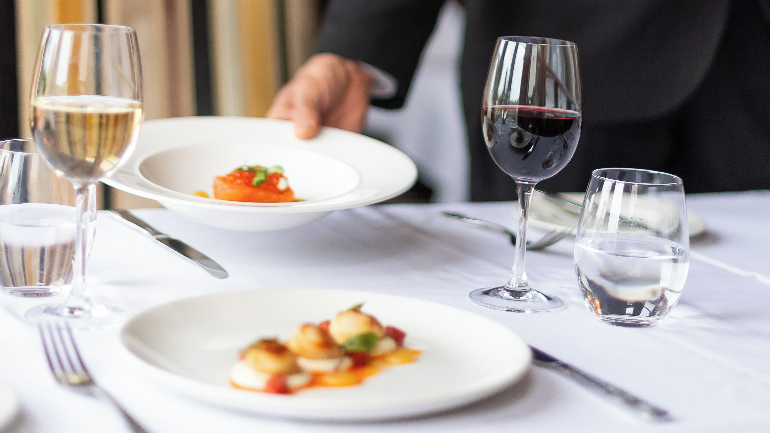 A dining table with plates of food, wine glasses, and a water glass.