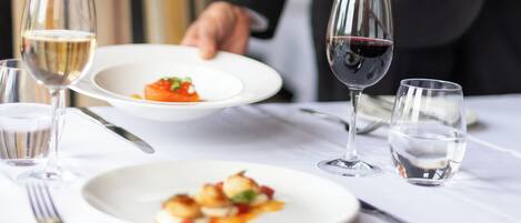 A dining table with plates of food, wine glasses, and a water glass.